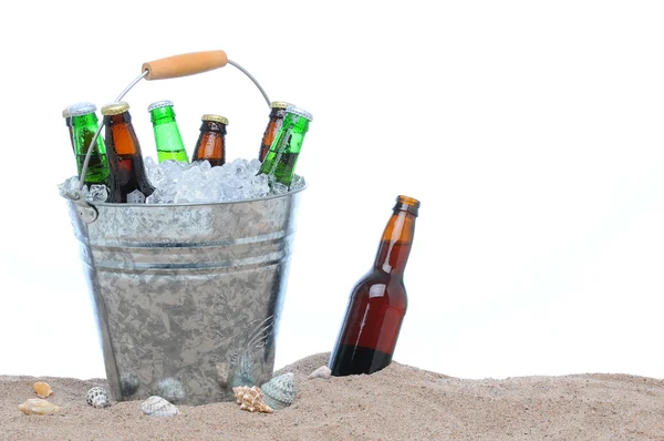 Assorterte ølflasker i en bøtte med is i sanden. – stockfoto