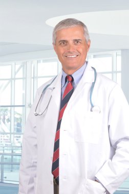 Smiling Middle Aged Male Doctor in Lab Coat with Stethoscope standing in a modern medical facility. clipart