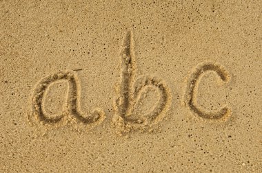 Alphabet letters handwritten in sand on beach clipart