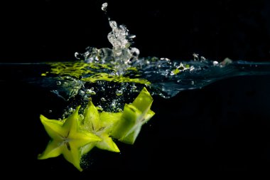 A trio of star fruit pieces create a splash as they hit the water clipart