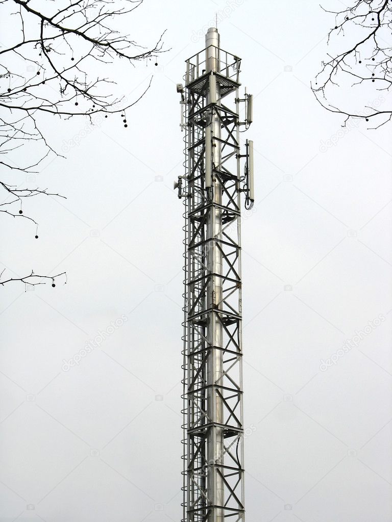 Metallic communication tower with antennas over sky background