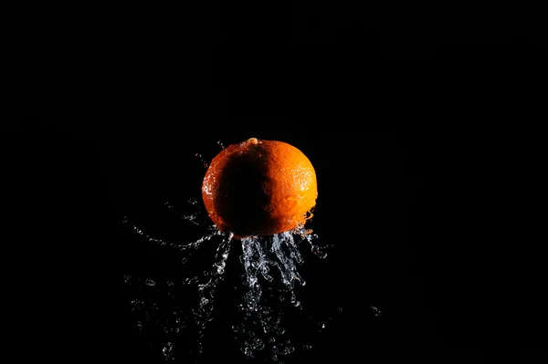 Narancs a víz csobbanás, a fekete háttér — Stock Fotó
