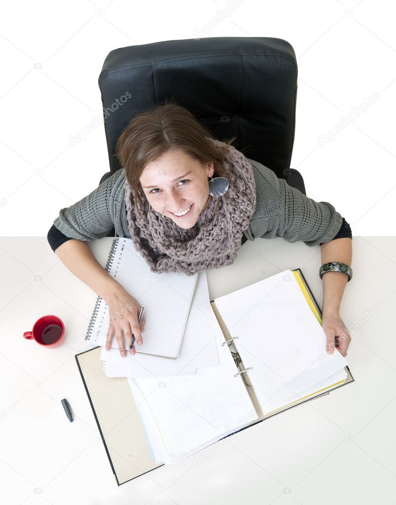 Young smiling female student looking up from the notes on her desk seen from above