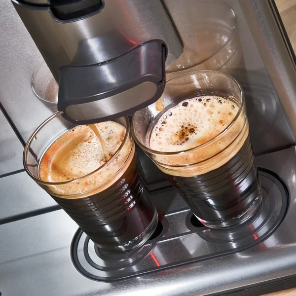 Pad coffee machine seen from above, brewing two glass cups of fresh, creamy coffee