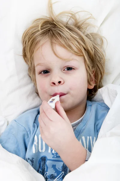インフルエンザでベッドに横たわって彼の温度を取って彼の口で温度計を持つ幼い子供 — ストック写真