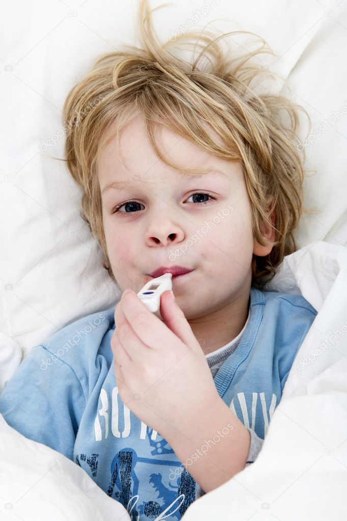 Young child with a thermometer in his mouth, taking his temperature, lying in bed with a flu