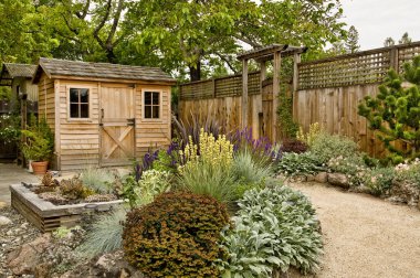 Beautifully landscaped backyard with small wooden shed, fence and pathway clipart