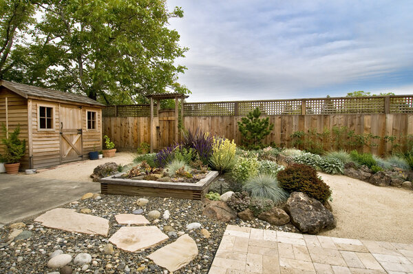 Beautifully landscaped backyard with small wooden shed, fence and pathway