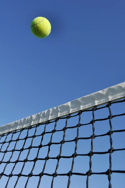 Žlutá tenisový míček letí přes síť — Stock fotografie