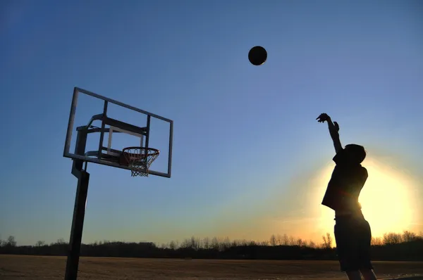 Silhouette eines Teenie-Jungen, der einen Basketball schießt — Stockfoto