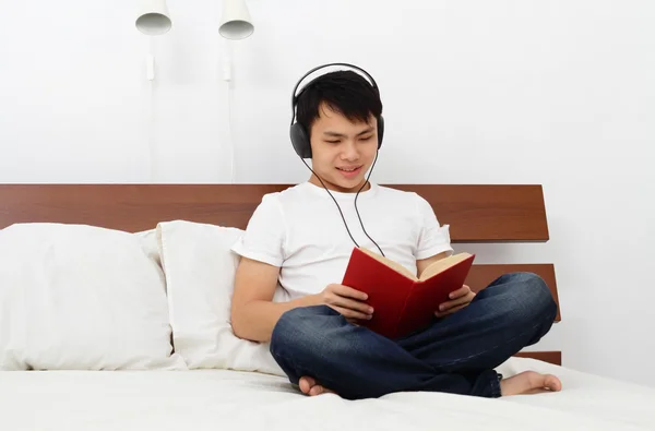 ベッドの上の本を読んで若いアジアの男 — ストック写真
