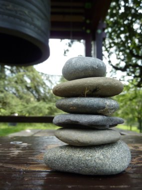 Zen stones on a peace of wood next to a japonese bell in a park clipart