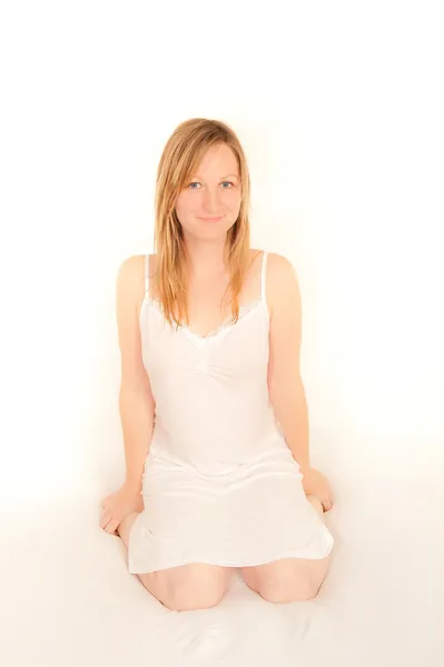 Cute young woman sitting on bed in her nightdress — Stock Photo, Image