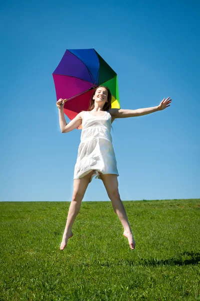 Happy young woman jumping with colorful umbrella — Stock Photo, Image