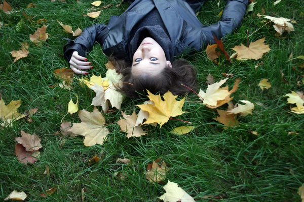 Mulher sorridente deitada em um tapete de folhas — Fotografia de Stock