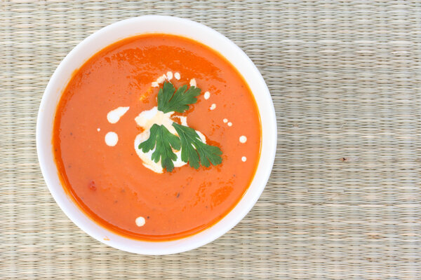 Top down view of red tomatoe soup in white bowl, sprinkled with cream