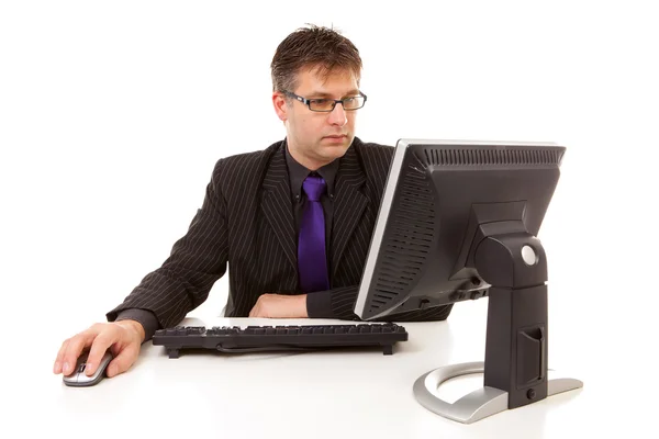Geschäftsmann sitzt bei der Arbeit hinterm Schreibtisch und blickt auf Monitor — Stockfoto
