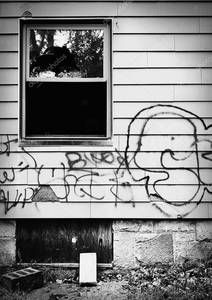 A run down abandoned house with broken window and graffiti.