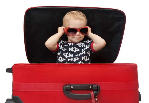 Petit enfant en lunettes de soleil regardant dehors valise rouge — Photo