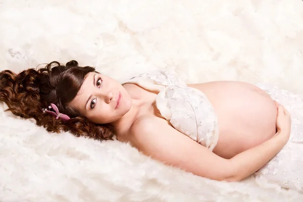 Pregnant woman lying on fur looking at camera. — Stock Photo, Image