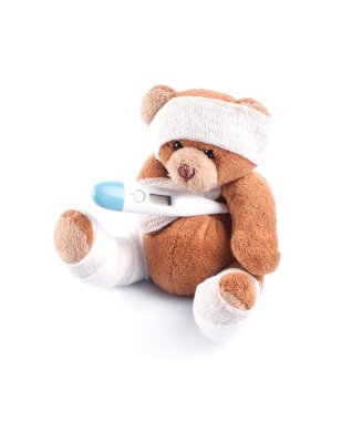 Sick teddy bear wrapped in bandages with underarm thermometer, isolated on white background