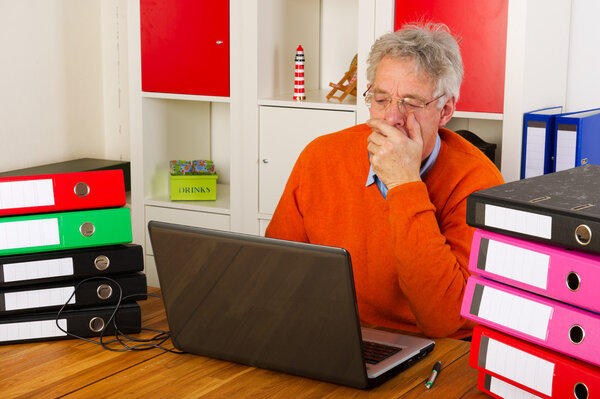 Elderly man is sitting with laptop and many paper folders