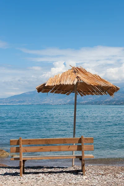 Греческий пляж с пустой скамейкой — стоковое фото