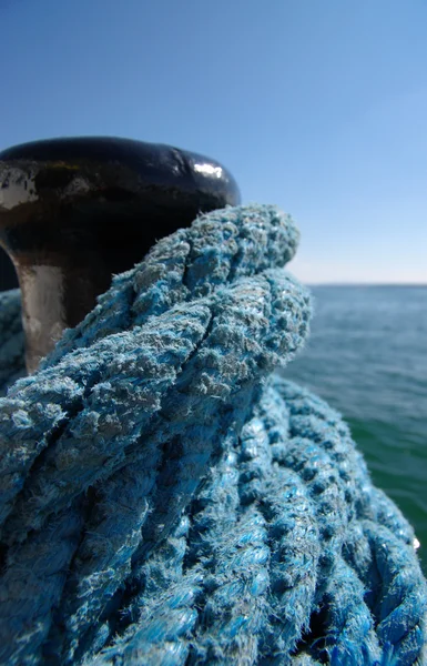 stock image Black bollard and blue rope coils with blurry background, vertical.