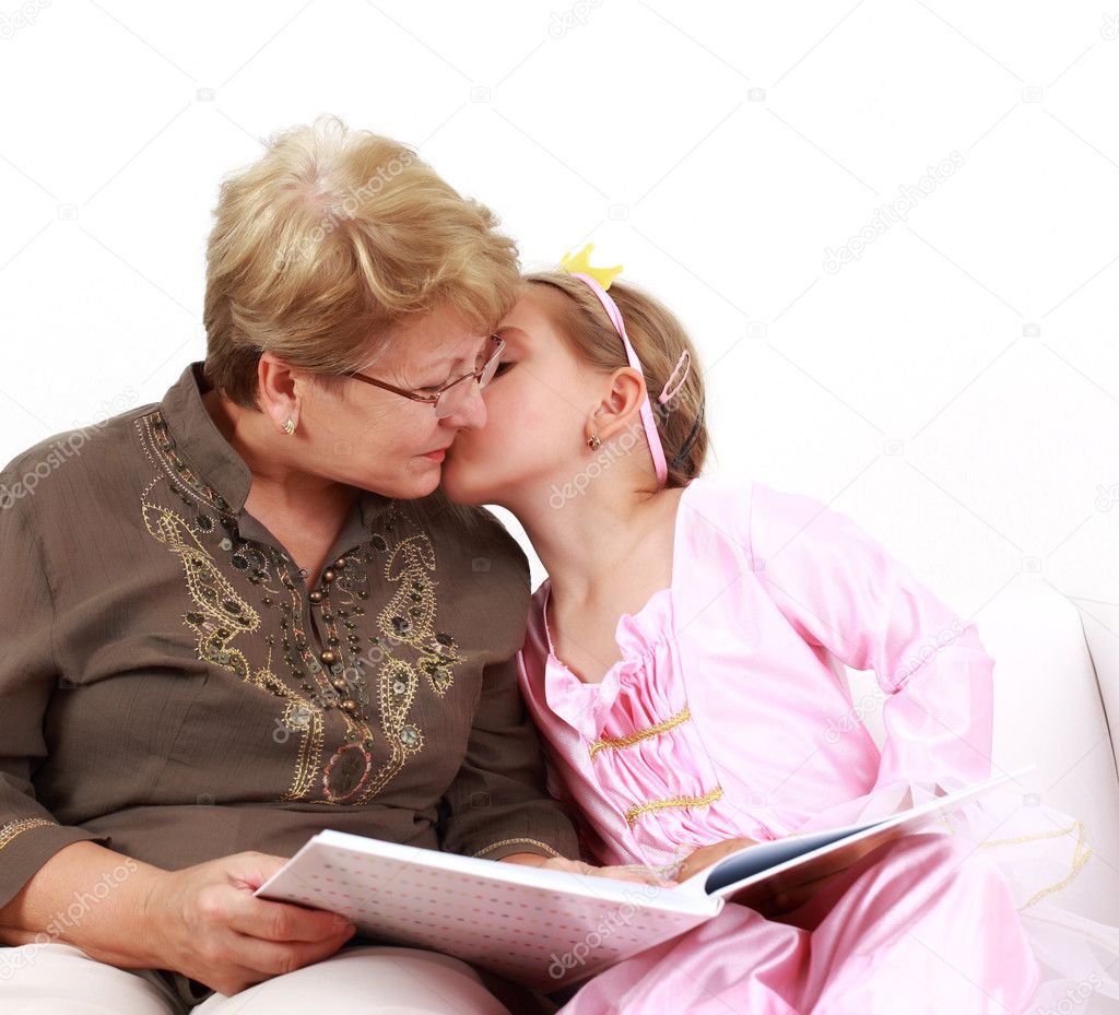Cute little girl reading with grandmother and giving a kiss
