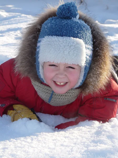Der Junge lag in der hellen Winterkleidung auf dem Schnee — Stockfoto