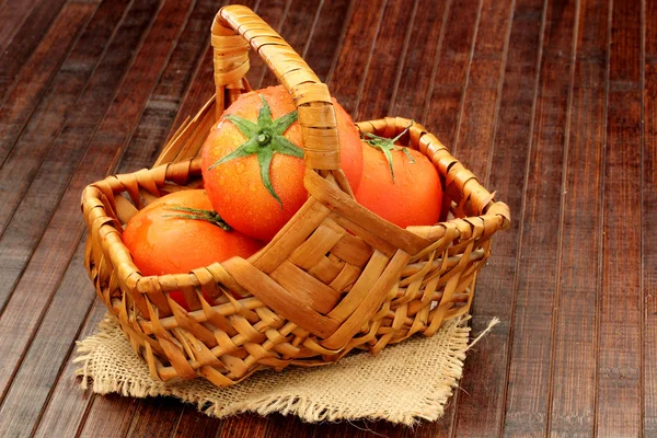 Tomates em uma cesta em um fundo de madeira — Fotografia de Stock