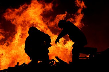 Two silhouetted firemen fighting a large fire clipart