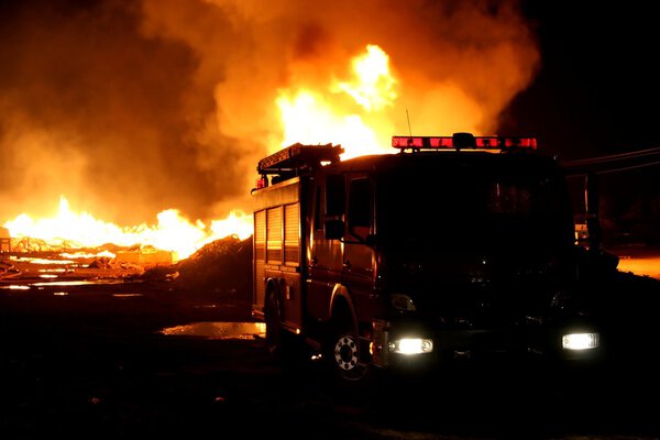 A firetruck in front of a blazing fire at night