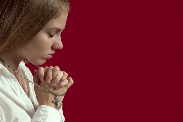 用一个十字架祈祷的银链上穿白衬衫的年轻女子 红色背景上 — 图库照片