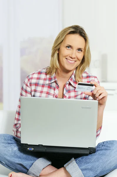 Mladá žena sedí na pohovce s počítačem a kreditní karty — Stock fotografie