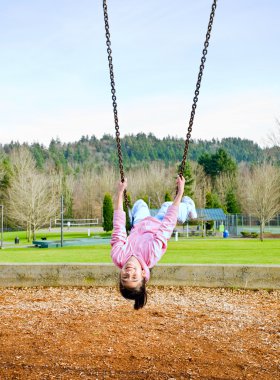 Happy little nine year old part Asian girl on the swings at park clipart