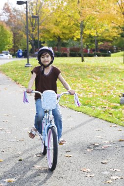 Little girl riding bike in park clipart