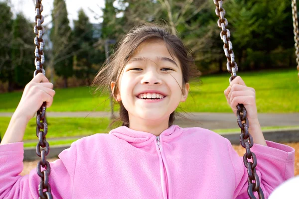 Menina feliz sorrindo em um balanço no parque — Fotografia de Stock