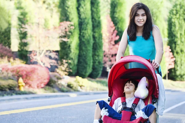 Teenie-Mädchen schubst ihren kleinen Bruder im Kinderwagen — Stockfoto