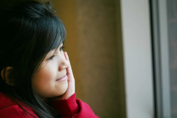 Malá Asijská dívka tiše sedět u okna, ruku na bradu — Stock fotografie