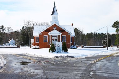 An old snowed in church sitting in the middle of the fork in the road after a snowstorm with room for your text. clipart