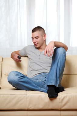 Young man using a cell phone at home clipart