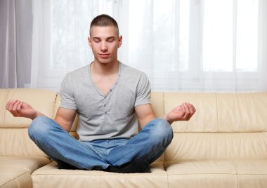 Handsome man making yoga on the sofa clipart