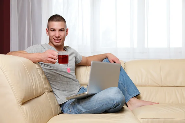Beau homme avec ordinateur portable et thé à la maison — Photo
