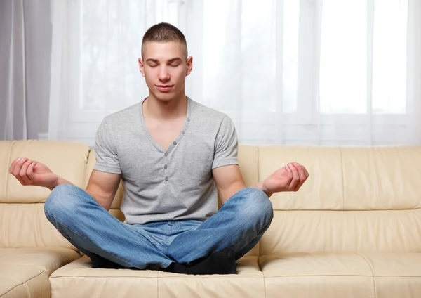 Schöner Mann macht Yoga auf dem Sofa lizenzfreie Stockbilder