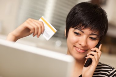 Multiethnic Woman Holding Phone and Credit Card Using Laptop clipart