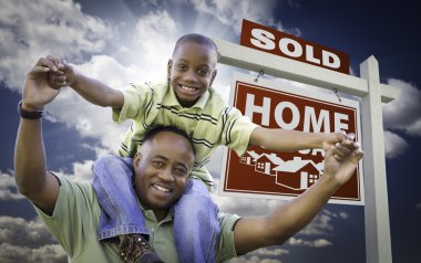 Happy African American Father with Son In Front of Sold Home For Sale Real Estate Sign and Sky. clipart