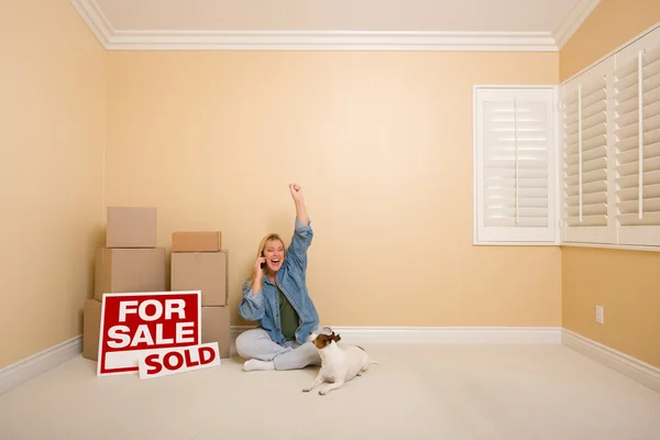 使用电话庆祝旁边移动框 出售的房地产标志和狗在空房间的地板上坐在漂亮女人 — 图库照片