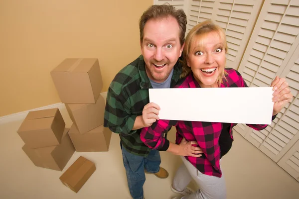 Casal feliz segurando sinal em branco no quarto com caixas embaladas — Fotografia de Stock