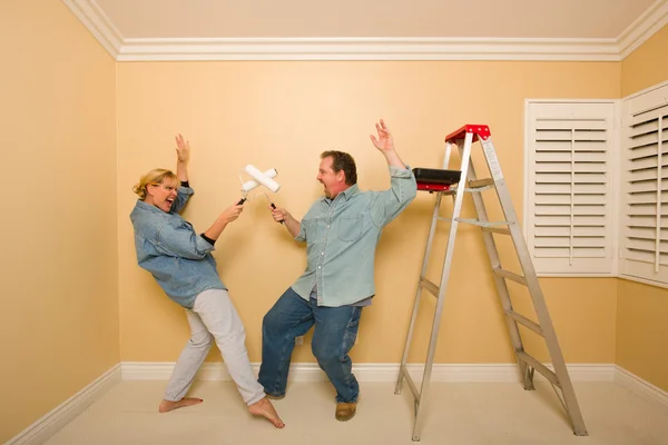 Casal divertido jogando luta de espadas com rolos de pintura — Fotografia de Stock